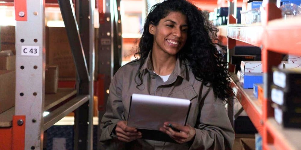 Brown-haired warehouse female worker smiles while overseeing inventory accuracy.