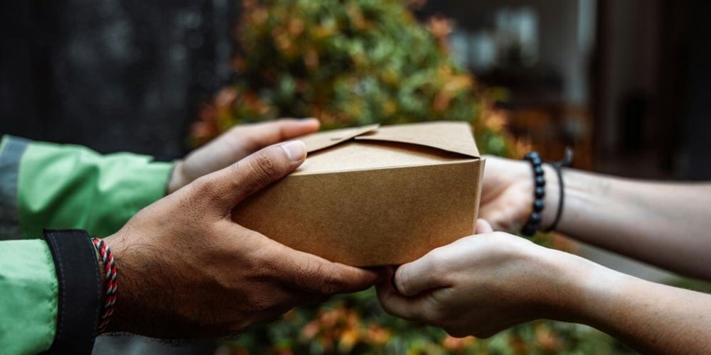 Hands passing a delivery box, representing seamless omnichannel fulfillment strategies.